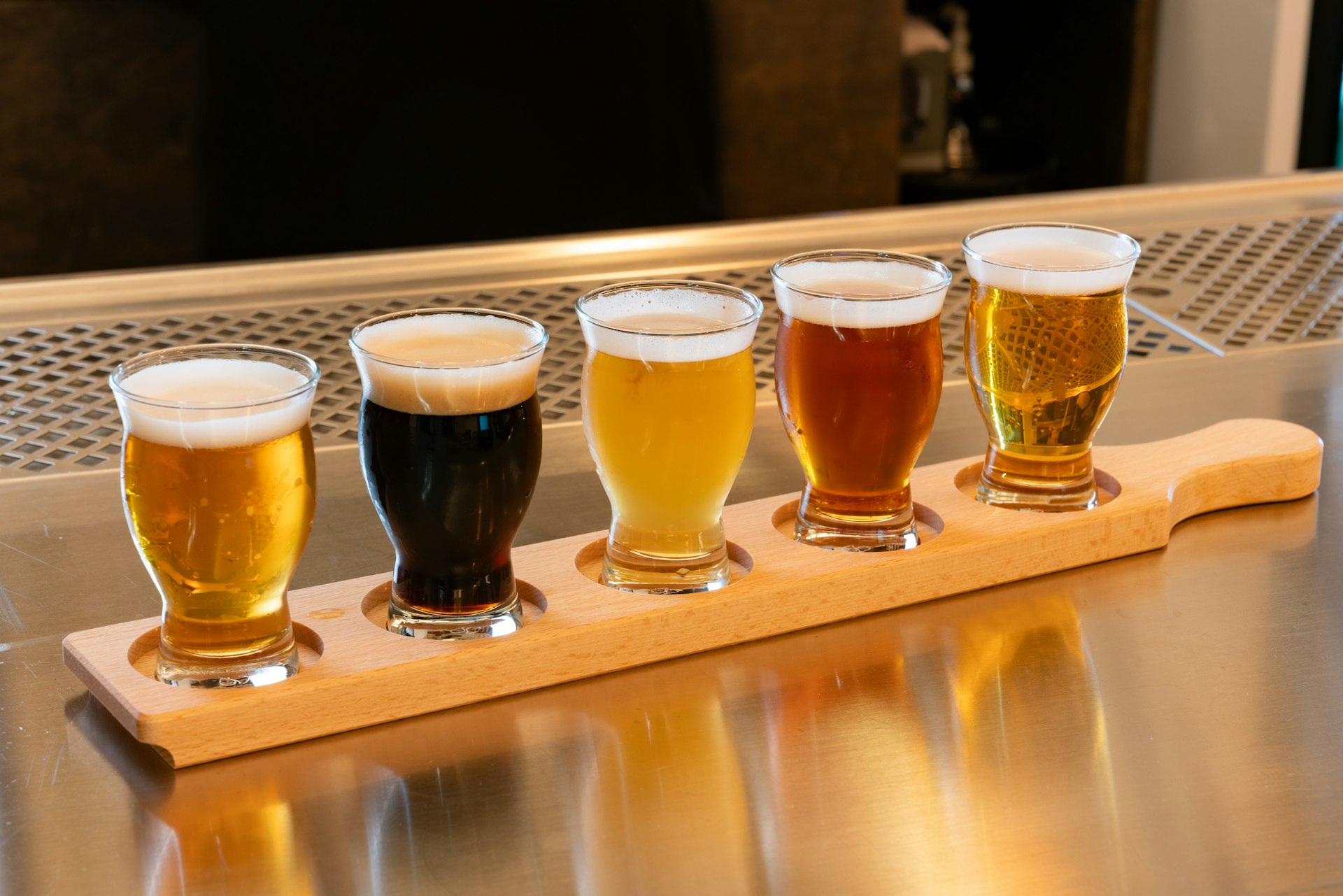 A flight of five beverage samples in tasting glasses on a wooden paddle, ranging from pale to dark — the kind of sample lineup a Halocline sensory panel evaluates